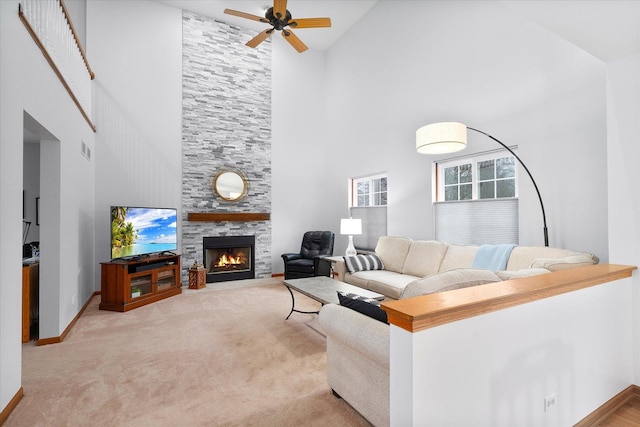 carpeted living area with visible vents, a high ceiling, a tiled fireplace, ceiling fan, and baseboards