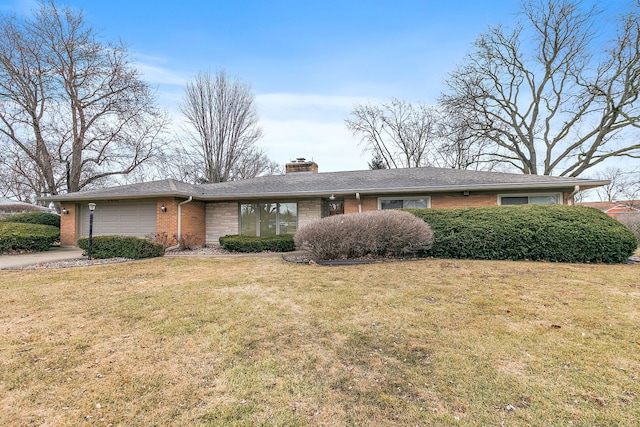 view of front of home with an attached garage, brick siding, driveway, a front lawn, and a chimney