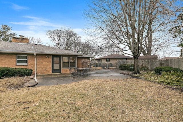 back of property featuring a patio, brick siding, a shingled roof, fence, and a chimney