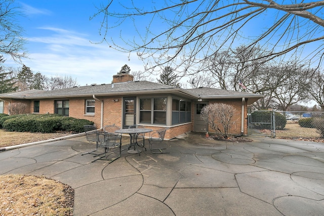 rear view of house with a patio, a chimney, a gate, fence, and brick siding