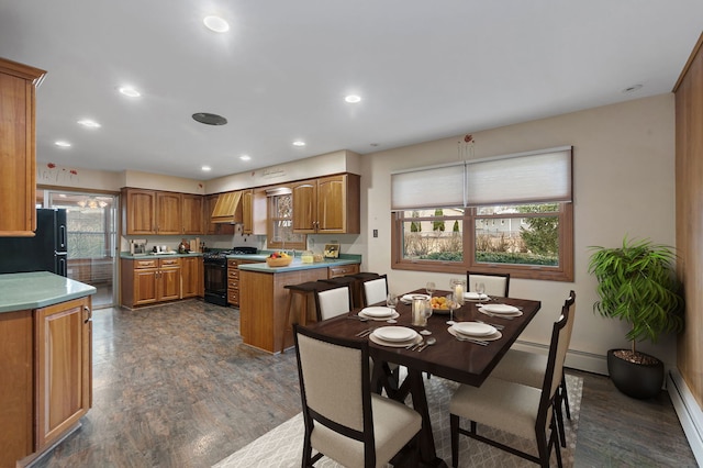 kitchen with dark wood-style floors, brown cabinetry, a baseboard heating unit, a peninsula, and black appliances