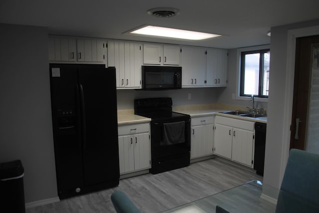 kitchen featuring light countertops, visible vents, a sink, light wood-type flooring, and black appliances