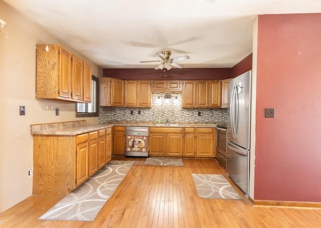 kitchen with brown cabinetry, light wood-style flooring, stainless steel appliances, light countertops, and backsplash