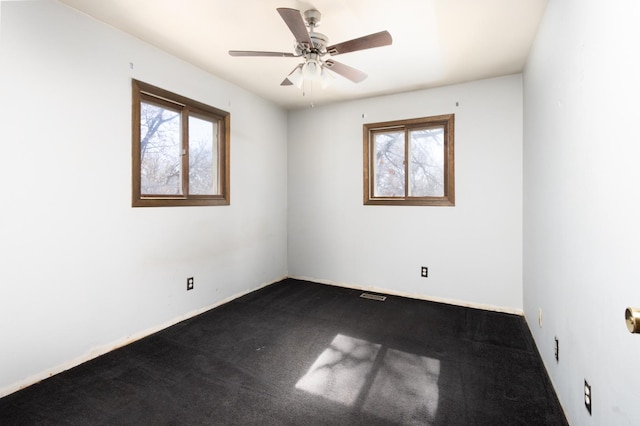 empty room with a healthy amount of sunlight, dark colored carpet, and a ceiling fan