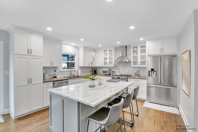 kitchen with high quality appliances, a center island, wall chimney range hood, white cabinetry, and a sink