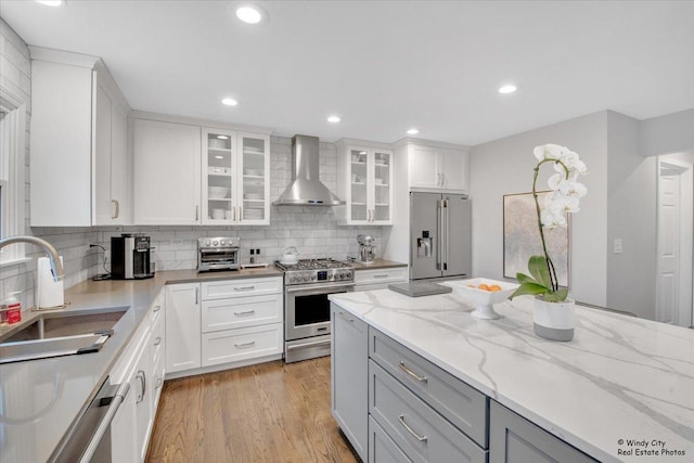 kitchen featuring high end appliances, a sink, light wood-type flooring, wall chimney range hood, and backsplash