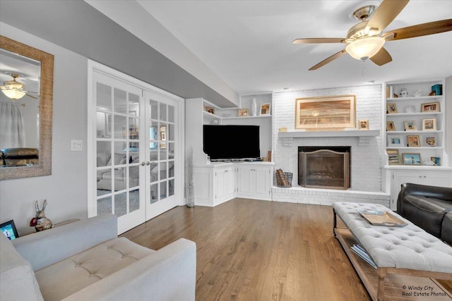 living room with french doors, a brick fireplace, wood finished floors, and built in features