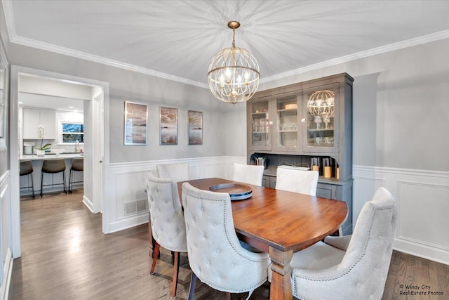 dining area featuring dark wood-style flooring, visible vents, ornamental molding, wainscoting, and a chandelier