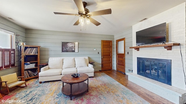 living room with visible vents, a fireplace, wood finished floors, and a ceiling fan