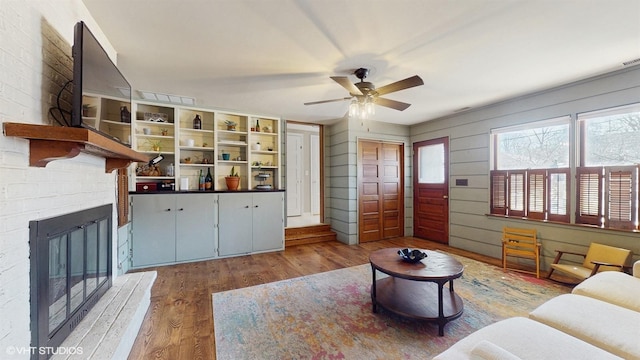 living room with ceiling fan, a brick fireplace, and wood finished floors