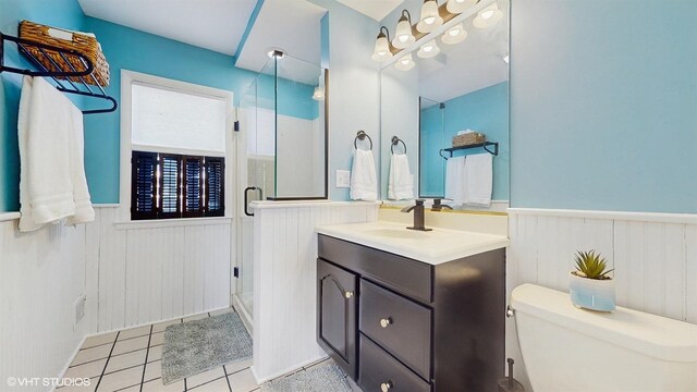 full bathroom with toilet, a shower stall, tile patterned flooring, wainscoting, and vanity