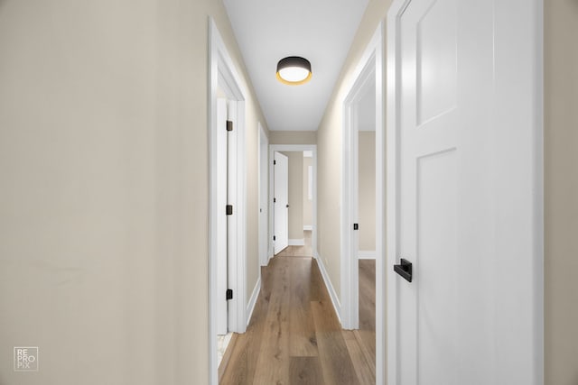 corridor featuring light wood-type flooring and baseboards