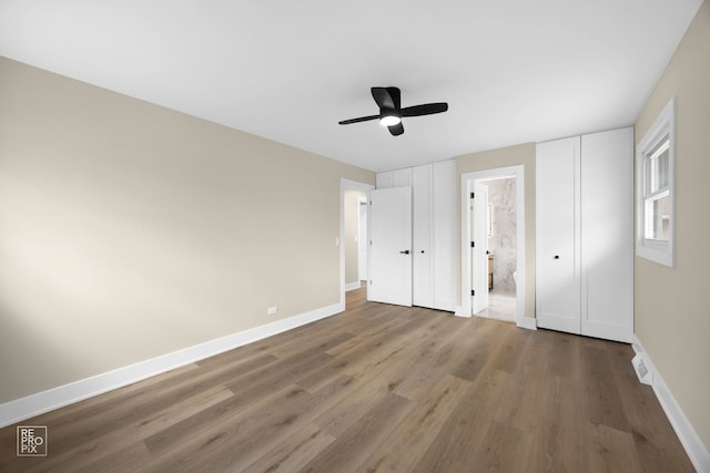 unfurnished bedroom with a ceiling fan, wood finished floors, baseboards, and two closets