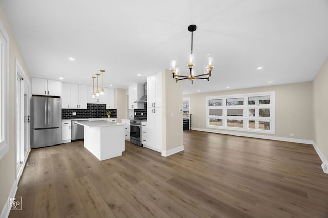 kitchen with open floor plan, a center island, appliances with stainless steel finishes, wall chimney range hood, and decorative backsplash