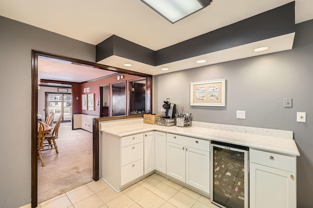 kitchen featuring wine cooler, light colored carpet, light tile patterned floors, a peninsula, and white cabinetry