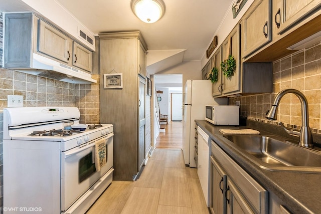 kitchen featuring white appliances, a sink, under cabinet range hood, dark countertops, and backsplash