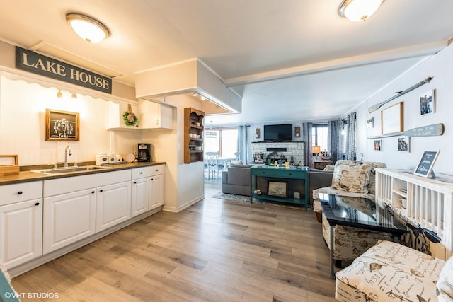 kitchen featuring a sink, dark countertops, light wood-style floors, white cabinets, and a fireplace