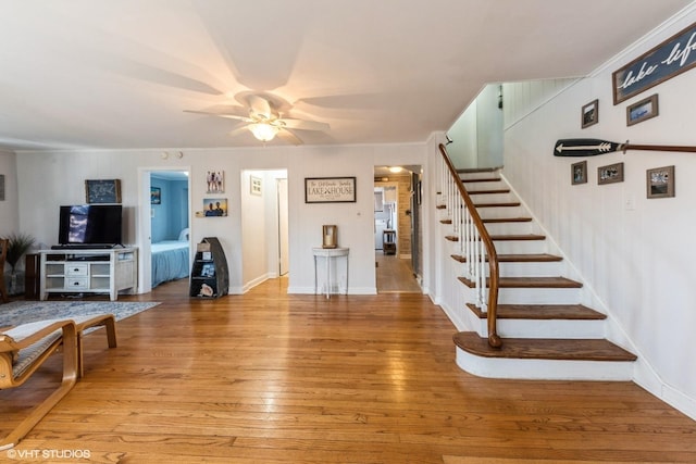 living room featuring light wood finished floors, stairway, crown molding, and a ceiling fan