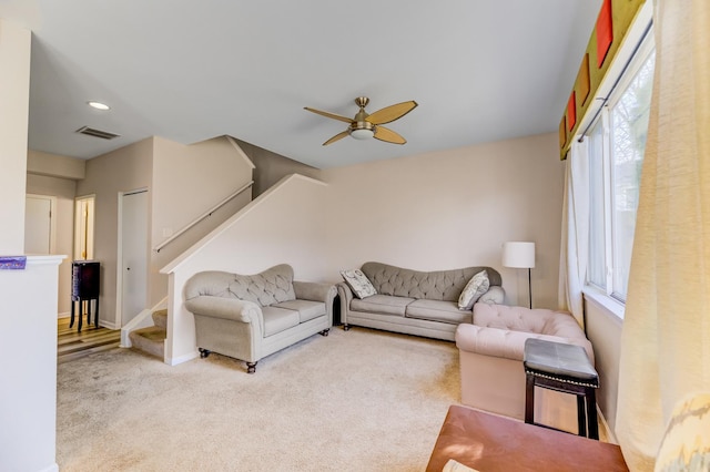 carpeted living room featuring stairs, baseboards, visible vents, and a ceiling fan