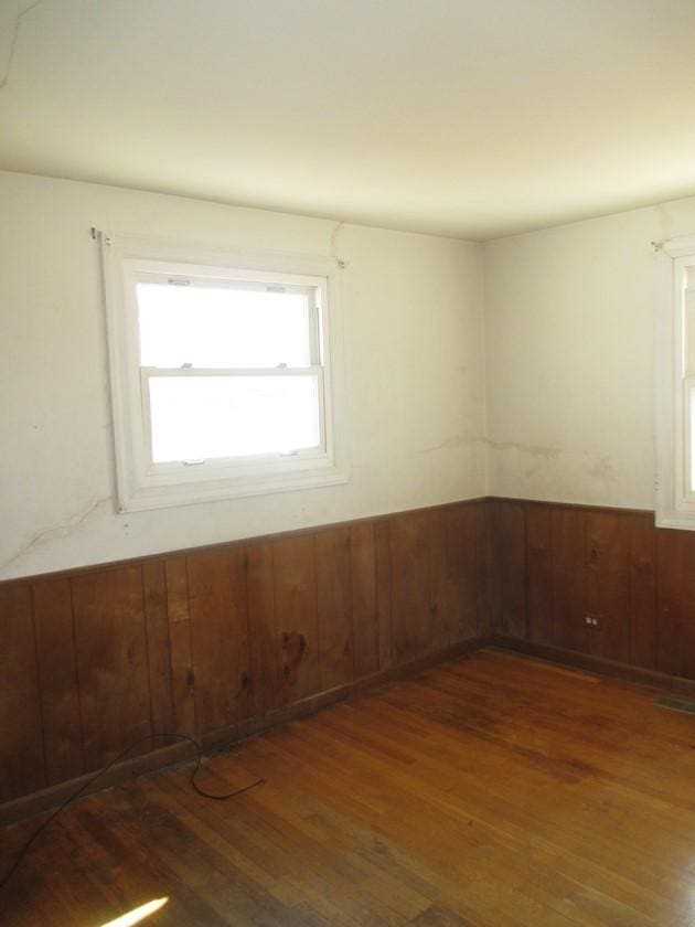 unfurnished room with a wainscoted wall, wood walls, and wood finished floors