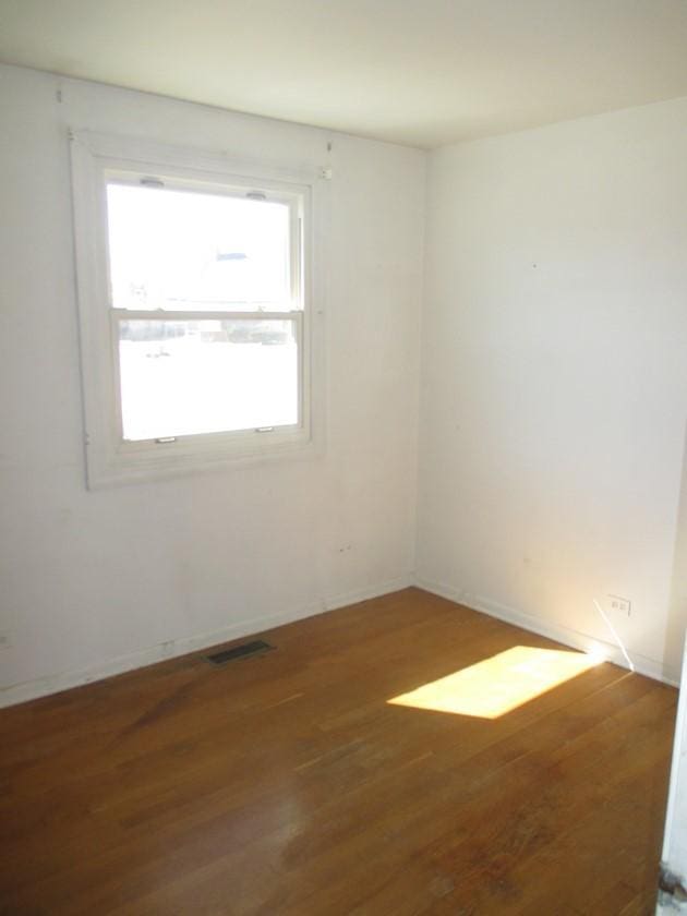 empty room featuring wood finished floors, visible vents, and baseboards