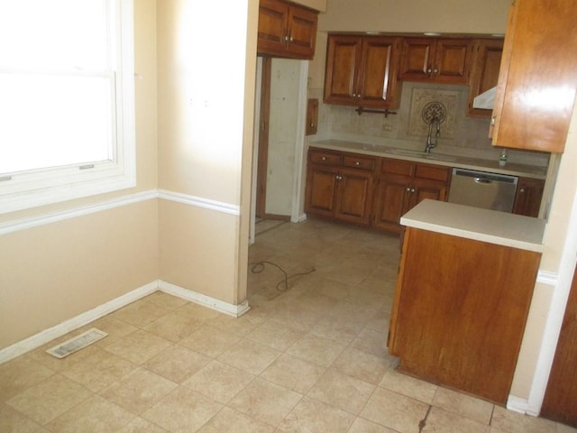 kitchen featuring brown cabinets, light countertops, backsplash, stainless steel dishwasher, and baseboards