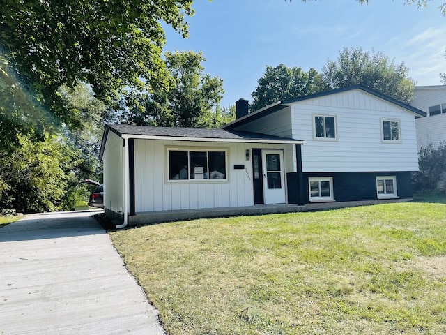 tri-level home featuring a chimney, a front lawn, board and batten siding, and concrete driveway