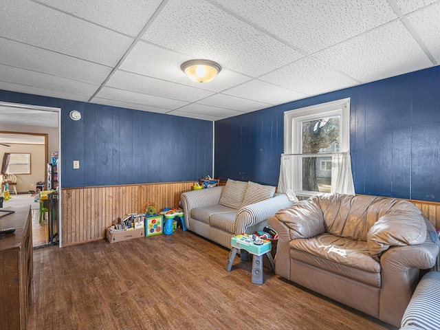 living area with wood walls, a drop ceiling, and wood finished floors