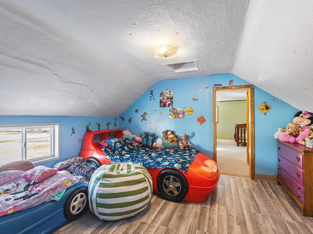 bedroom with lofted ceiling, a textured ceiling, and wood finished floors