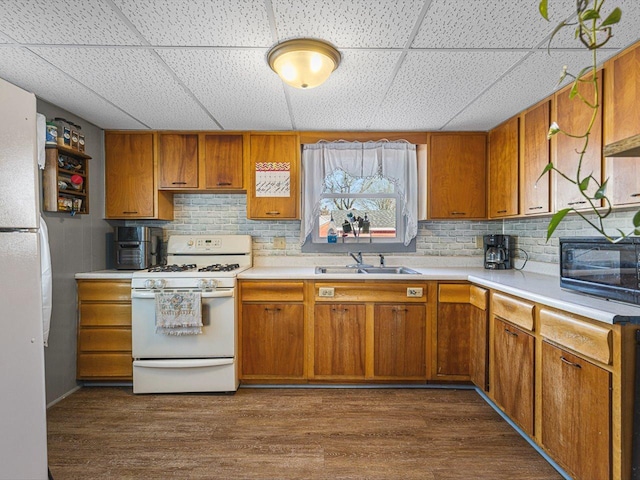 kitchen with white appliances, dark wood finished floors, brown cabinetry, and a sink