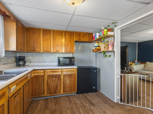 kitchen featuring refrigerator, black microwave, light countertops, and dark wood finished floors