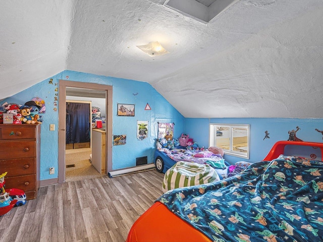 bedroom featuring vaulted ceiling, a textured ceiling, baseboards, and wood finished floors