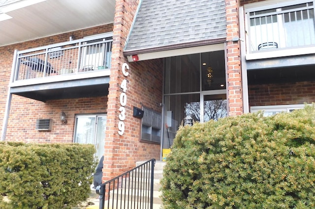 view of side of home with a balcony, brick siding, mansard roof, and roof with shingles