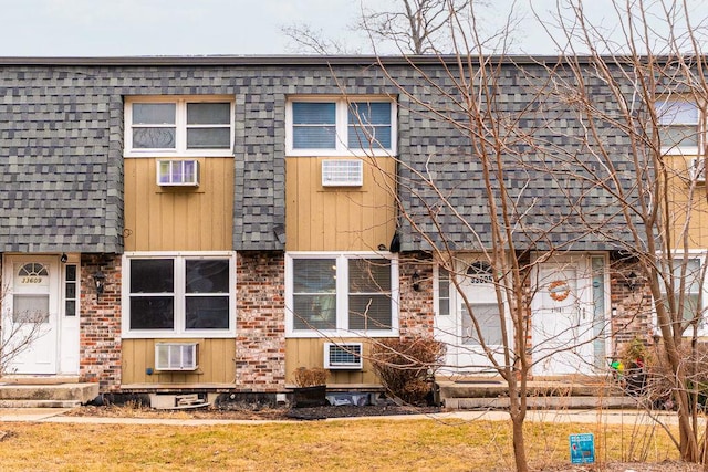 townhome / multi-family property with entry steps, mansard roof, brick siding, roof with shingles, and a wall mounted air conditioner