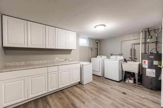 clothes washing area with cabinet space, washer and clothes dryer, light wood-style flooring, water heater, and a sink