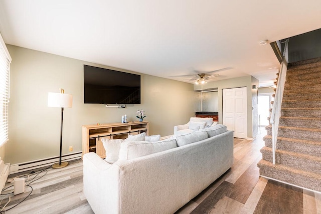 living area featuring a baseboard heating unit, light wood-type flooring, stairs, and a ceiling fan