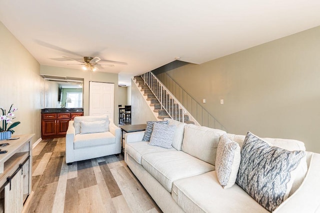 living room with stairs, ceiling fan, and light wood-type flooring