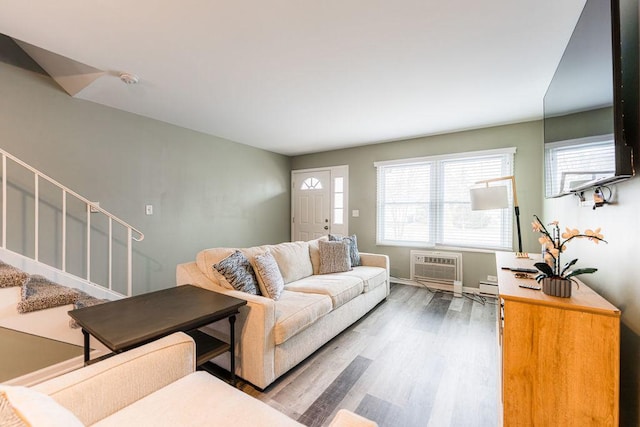 living area featuring a wall unit AC, a baseboard heating unit, wood finished floors, baseboards, and stairs