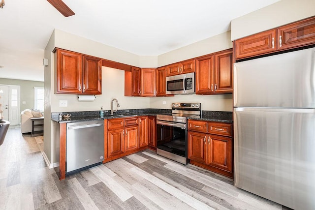 kitchen featuring dark stone counters, stainless steel appliances, light wood finished floors, and a sink