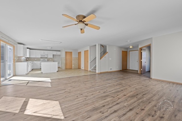 unfurnished living room with stairs, light wood finished floors, a sink, and baseboards