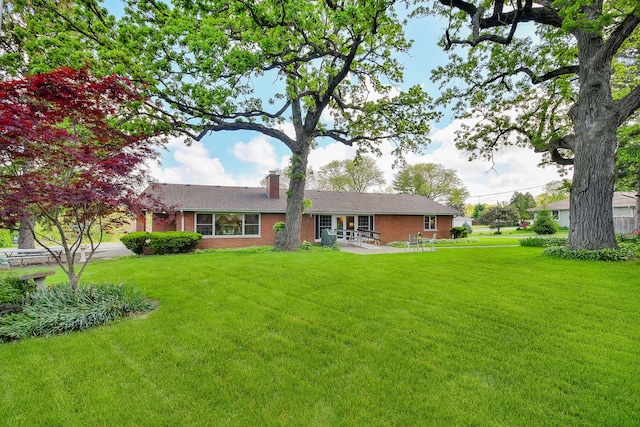 view of front of home with a front lawn, a chimney, brick siding, and a patio