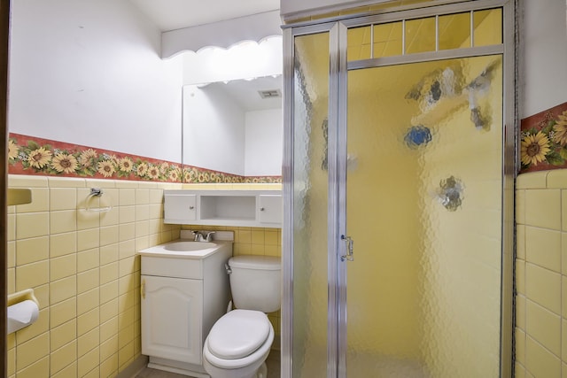 full bath featuring tile walls, a shower stall, toilet, vanity, and wainscoting