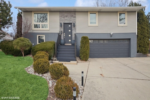 split foyer home featuring driveway, an attached garage, a front lawn, and stucco siding