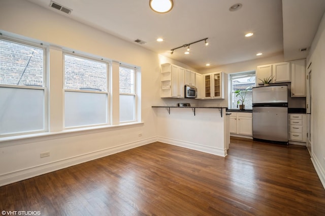 kitchen with dark countertops, visible vents, stainless steel appliances, and glass insert cabinets