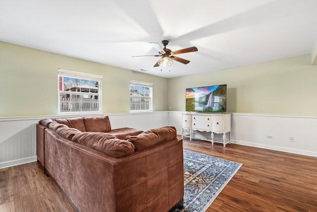 living room with a wainscoted wall, wood finished floors, and a ceiling fan