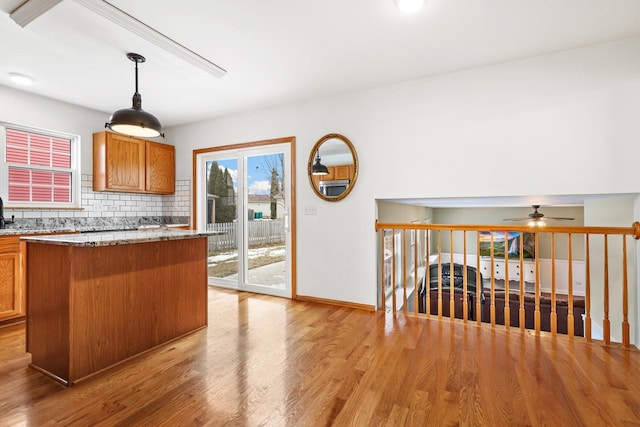 kitchen with light wood-style flooring, decorative backsplash, light stone countertops, brown cabinetry, and pendant lighting