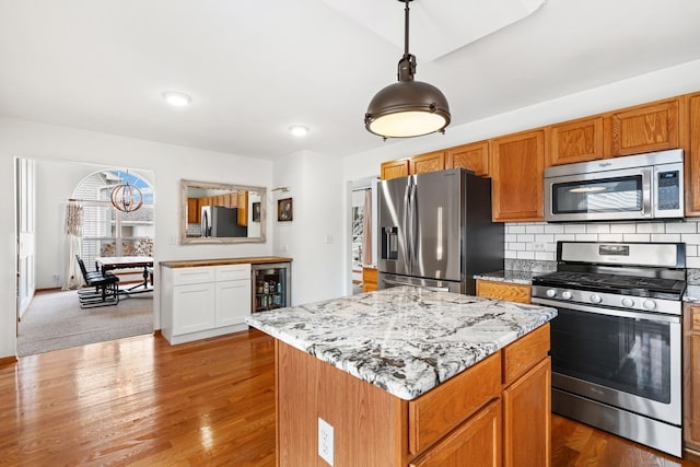 kitchen with wood finished floors, appliances with stainless steel finishes, backsplash, and light stone counters