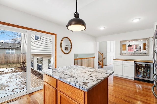 kitchen featuring light stone counters, beverage cooler, visible vents, light wood finished floors, and decorative light fixtures