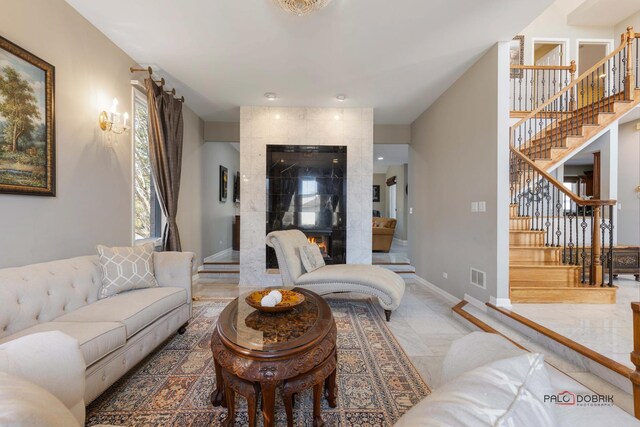 living area with stairs, a tiled fireplace, baseboards, and visible vents