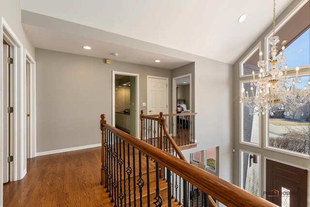 hall with an upstairs landing, a notable chandelier, wood finished floors, recessed lighting, and baseboards